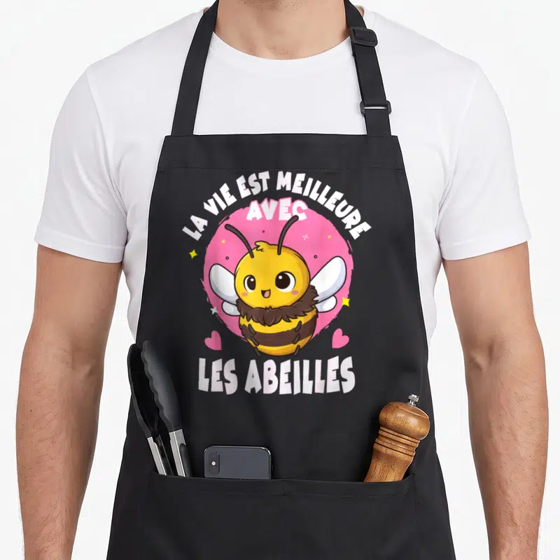 Tablier de cuisine noir avec une abeille jaune souriante, des cœurs roses et le texte La vie est meilleure avec les abeilles.