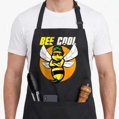 Tablier de cuisine noir avec une abeille stylisée portant casquette, lunettes et cigarette sur fond orange.