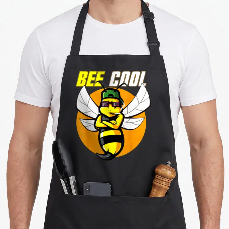 Tablier de cuisine noir avec une abeille stylisée portant casquette, lunettes et cigarette sur fond orange.