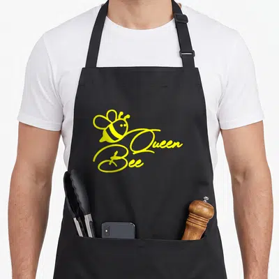 Tablier de cuisine noir avec illustration jaune d'une reine abeille et le texte cursive Queen Bee imprimé au centre.