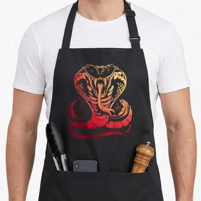 Tablier de cuisine noir avec illustration d'un cobra aux couleurs chaudes rouge et orange, gueule ouverte et langue fourchue visible.