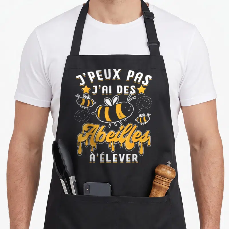 Tablier de cuisine noir avec inscription J'ai des Abeilles à Élever et illustration d'abeilles jaunes souriantes.