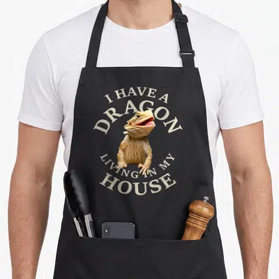 Tablier de cuisine noir avec un dragon barbu beige et le texte I HAVE A DRAGON LIVING IN MY HOUSE en lettres claires.