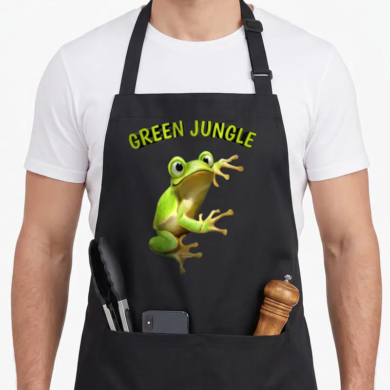 Tablier de cuisine noir avec une grenouille verte 3D et l'inscription Green Jungle en lettres jaunes.