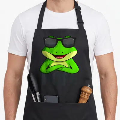 Tablier de cuisine noir avec une grenouille verte souriante portant des lunettes noires et le texte NOPE en dessous.