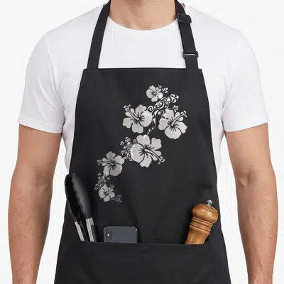 Tablier de cuisine noir avec lézards tribaux polynésiens et fleurs d'hibiscus stylisées en blanc.