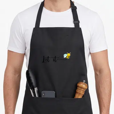 Tablier de cuisine noir avec inscription Let it Bee et abeille jaune souriante aux ailes bleues.