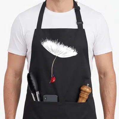Tablier de cuisine noir avec une coccinelle rouge suspendue à une graine de pissenlit blanche stylisée.