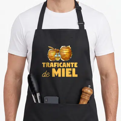Tablier de cuisine noir avec illustration de ruches et texte Traficante de Miel en orange doré.