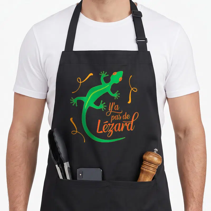 Tablier de cuisine noir avec un lézard vert stylisé et l'inscription Y a pas de Lézard en orange.