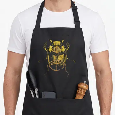 Tablier de cuisine noir avec illustration centrale d'un scarabée égyptien doré aux détails gravés.