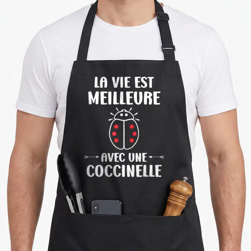 Tablier de cuisine noir avec une illustration de coccinelle rouge et le texte La vie est meilleure avec une coccinelle en blanc.