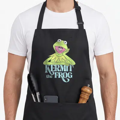 Tablier de cuisine noir avec une illustration vintage d'une grenouille verte souriante et du texte bleu clair.