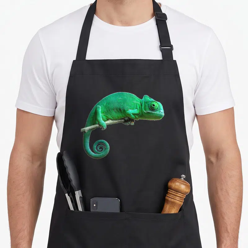 Tablier de cuisine noir avec un caméléon vert vif perché sur une brindille sèche au centre du torse.