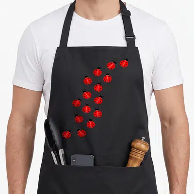 Tablier de cuisine noir avec plusieurs coccinelles rouges et noires à pois disposées en diagonale.