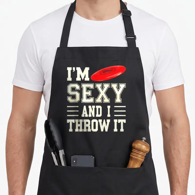 Tablier de cuisine noir avec texte blanc sexy et un disque rouge volant au-dessus.