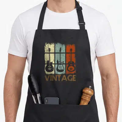 Tablier de cuisine noir avec illustration de trois guitares sur fonds colorés et le mot VINTAGE en bas.