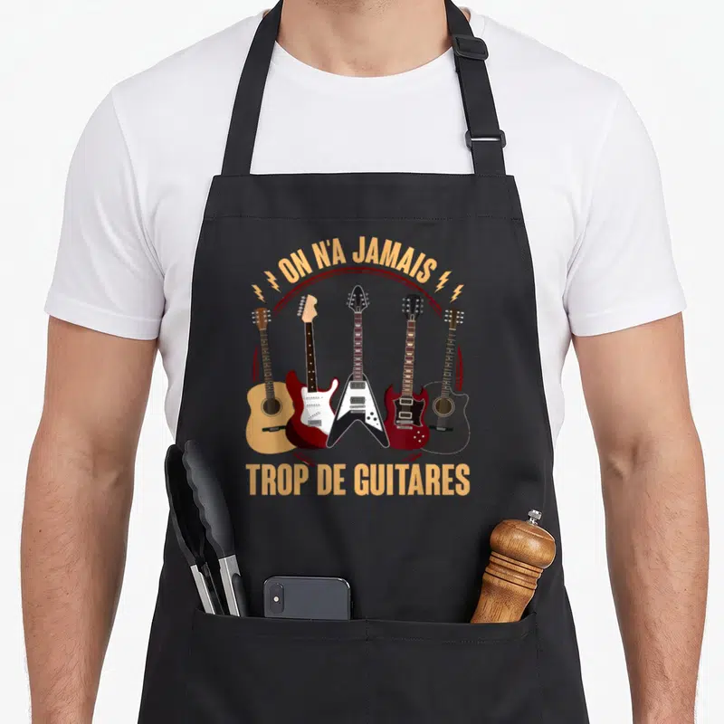 Tablier de cuisine noir avec cinq guitares et le texte on n'a jamais trop de guitares imprimé en orange et rouge.