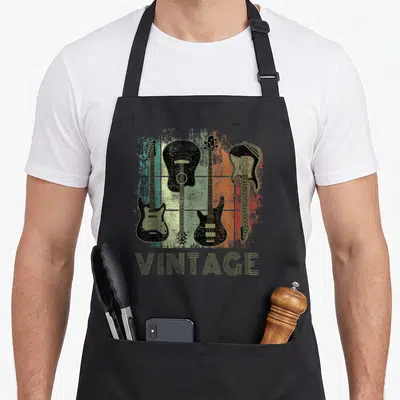Tablier de cuisine noir avec illustration de quatre guitares vintage sur fond coloré et le mot vintage en bas.