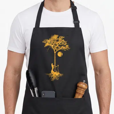 Tablier de cuisine noir avec illustration orange d'une guitare transformée en arbre de vie aux racines visibles.