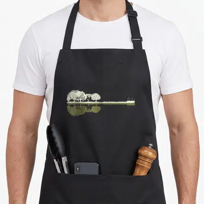 Tablier de cuisine noir avec une illustration blanche de forêts se reflétant dans l'eau verte.