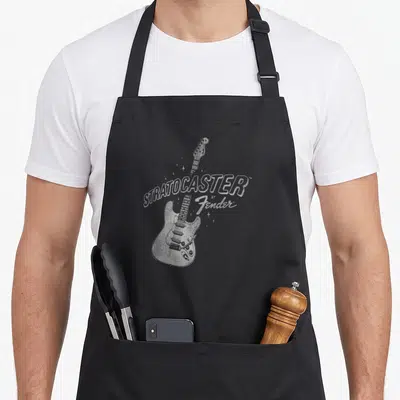 Tablier de cuisine noir avec une illustration blanche d'une guitare électrique et le texte STRATOCASTER by Fender entouré d'étoiles.