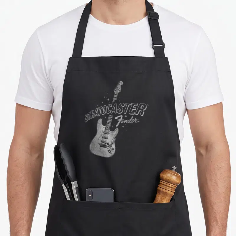 Tablier de cuisine noir avec une illustration blanche d'une guitare électrique et le texte STRATOCASTER by Fender entouré d'étoiles.