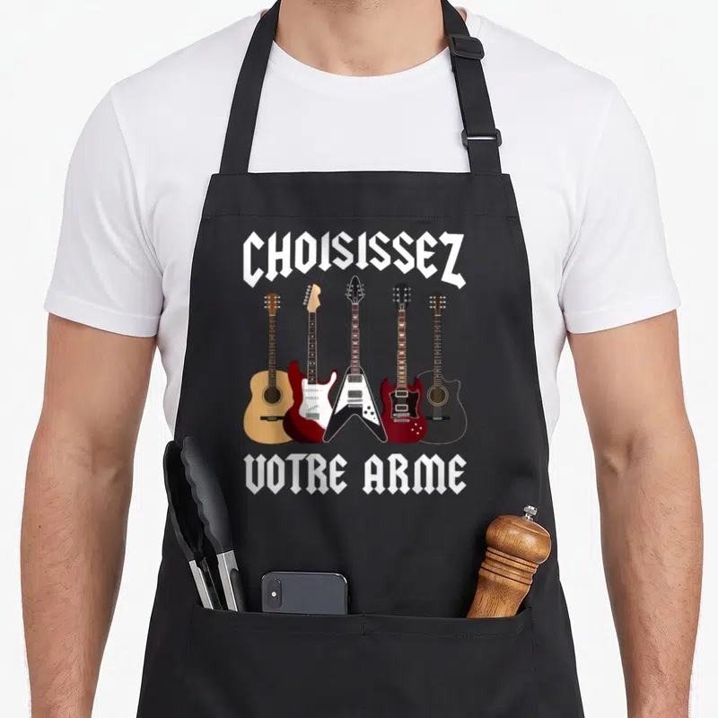 Tablier de cuisine noir avec cinq guitares imprimées et le texte Choisissez Votre Arme en typographie gothique blanche.