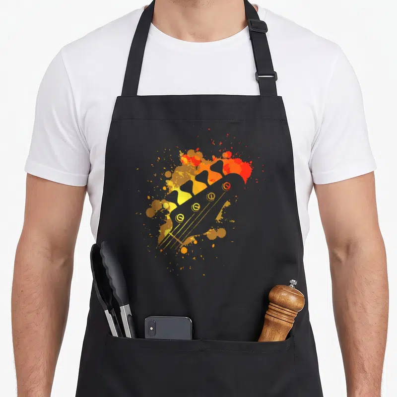 Tablier de cuisine noir avec illustration colorée d'une tête de guitare basse aux éclats orange et jaune.