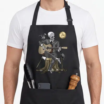 Tablier de cuisine noir avec un squelette en costume jouant de la guitare acoustique sur un tronc d'arbre sous une pleine lune.