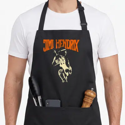 Tablier de cuisine noir avec une illustration vintage de Jimi Hendrix et son nom en lettres oranges au-dessus.
