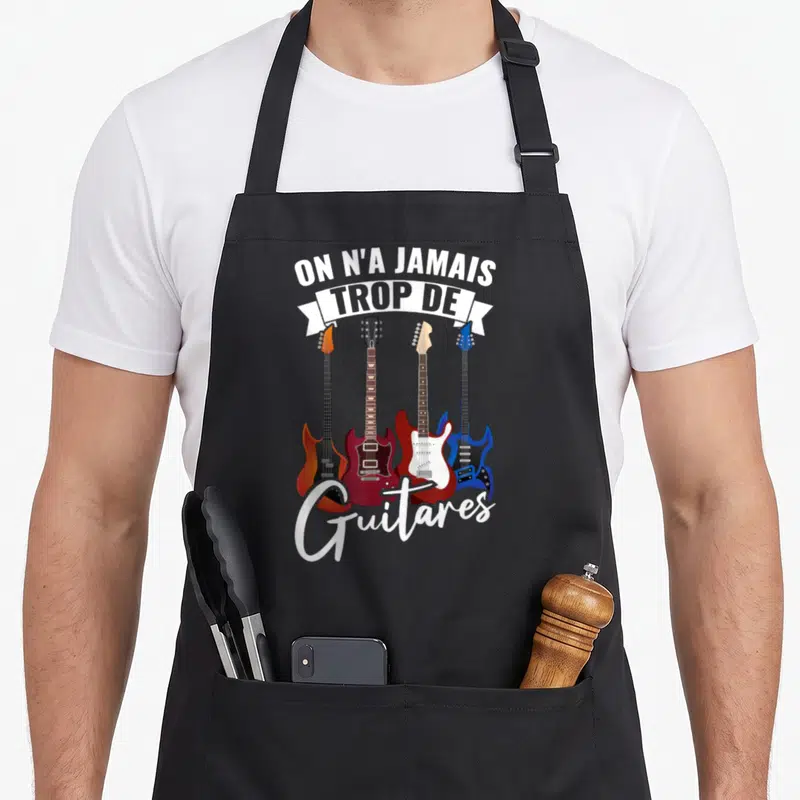 Tablier de cuisine noir avec quatre guitares électriques colorées et le texte On n'a jamais trop de Guitares imprimé en blanc.