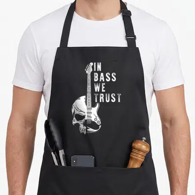 Tablier de cuisine noir avec un crâne fusionné à une guitare basse et le texte In Bass We Trust en blanc.