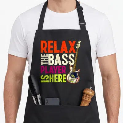 Tablier de cuisine noir avec texte multicolore Détendez-Vous Le Bassiste Est Ici et illustration de guitare basse.