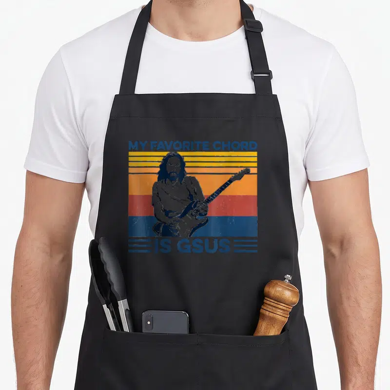 Tablier de cuisine noir avec illustration vintage d'un homme aux cheveux longs jouant d'une guitare électrique sur fond rayé coloré.