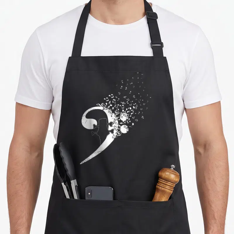 Tablier de cuisine noir avec une grande clé de fa blanche formant la silhouette d'un corps de guitare basse et des notes qui s'envolent.
