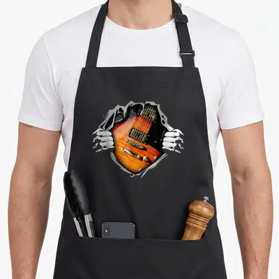 Tablier de cuisine noir avec illustration d'une guitare électrique orange et dorée sortant du tissu par des mains blanches.