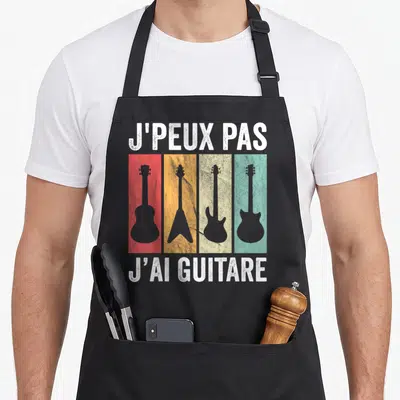 Tablier de cuisine noir avec quatre silhouettes de guitares colorées et texte blanc humoristique.