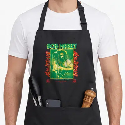 Tablier de cuisine noir avec une illustration colorée de Bob Marley jouant de la guitare sur fond vert et des textes Exodus en rouge.
