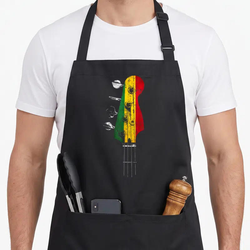 Tablier de cuisine noir avec une illustration de tête de basse aux couleurs vert jaune et rouge style reggae vintage.