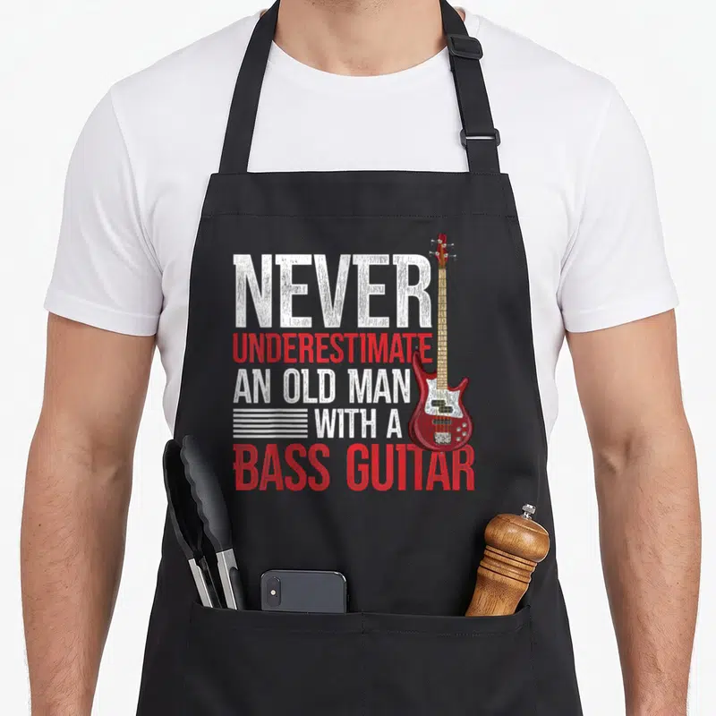Tablier de cuisine noir avec illustration d'une basse électrique rouge et texte blanc et rouge en anglais.