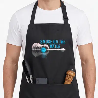 Tablier de cuisine noir avec illustration guitare formée d'arbres roses, lune bleue et texte Smoke on the Water en bleu.