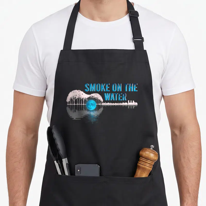 Tablier de cuisine noir avec illustration guitare formée d'arbres roses, lune bleue et texte Smoke on the Water en bleu.