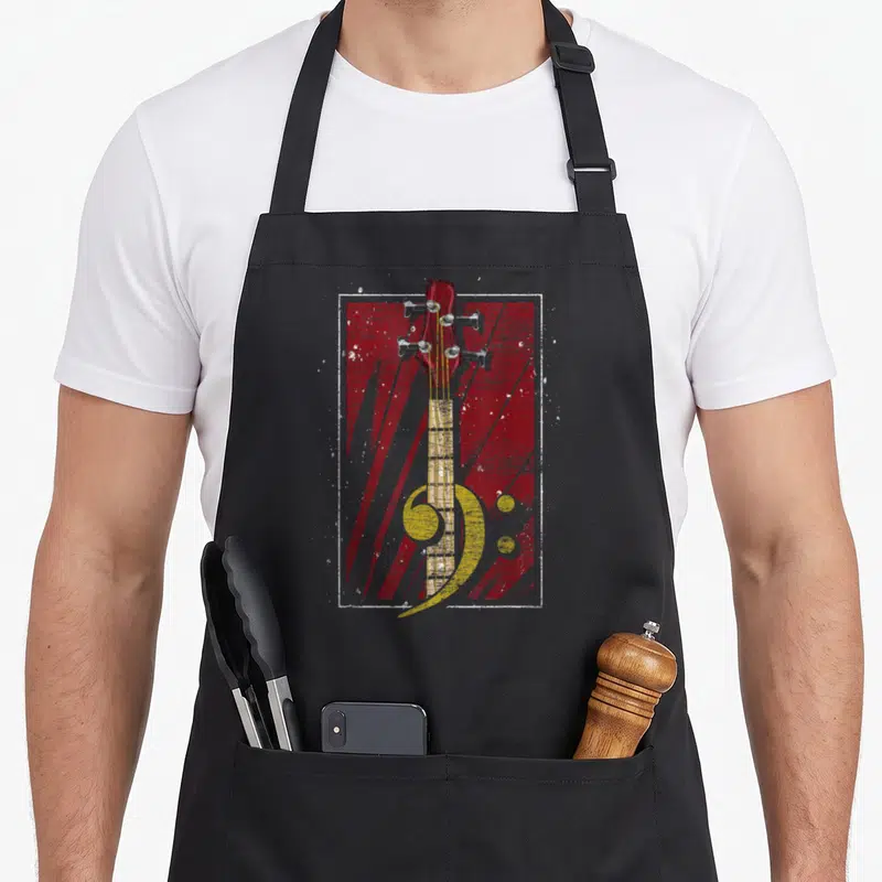 Tablier de cuisine noir avec tête de basse et clé de fa jaune sur fond rouge texturé.