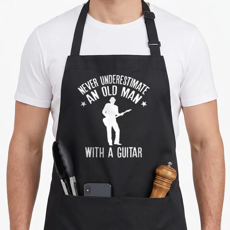 Tablier de cuisine noir avec silhouette blanche d'un musicien jouant de la guitare et texte humoristique en anglais.