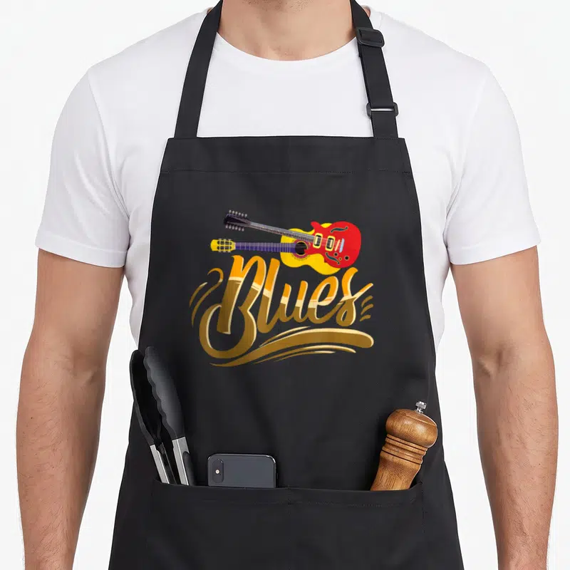Tablier de cuisine noir avec inscription Blues en lettres dorées et deux guitares colorées superposées au centre.
