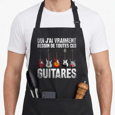 Tablier de cuisine noir avec cinq guitares électriques colorées et texte blanc distordu Oui j'ai vraiment besoin de toutes ces guitares.