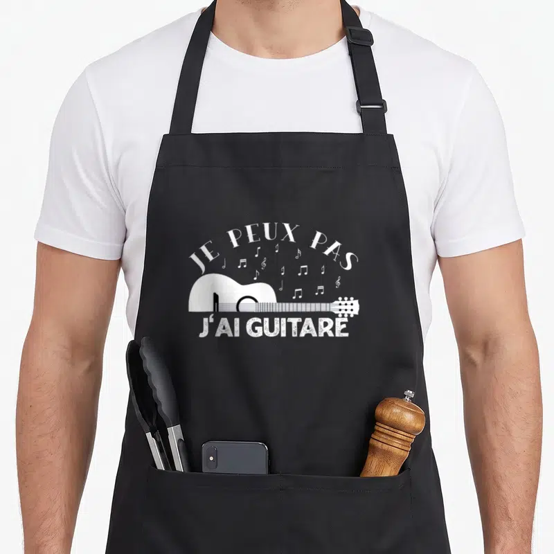Tablier de cuisine noir avec une illustration blanche de guitare acoustique et des notes de musique flottantes au-dessus du texte.