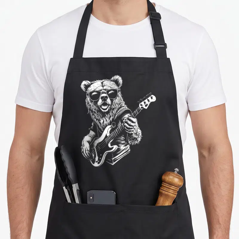 Tablier de cuisine noir avec illustration blanche d'un ours portant des lunettes de soleil et tenant une guitare basse électrique.