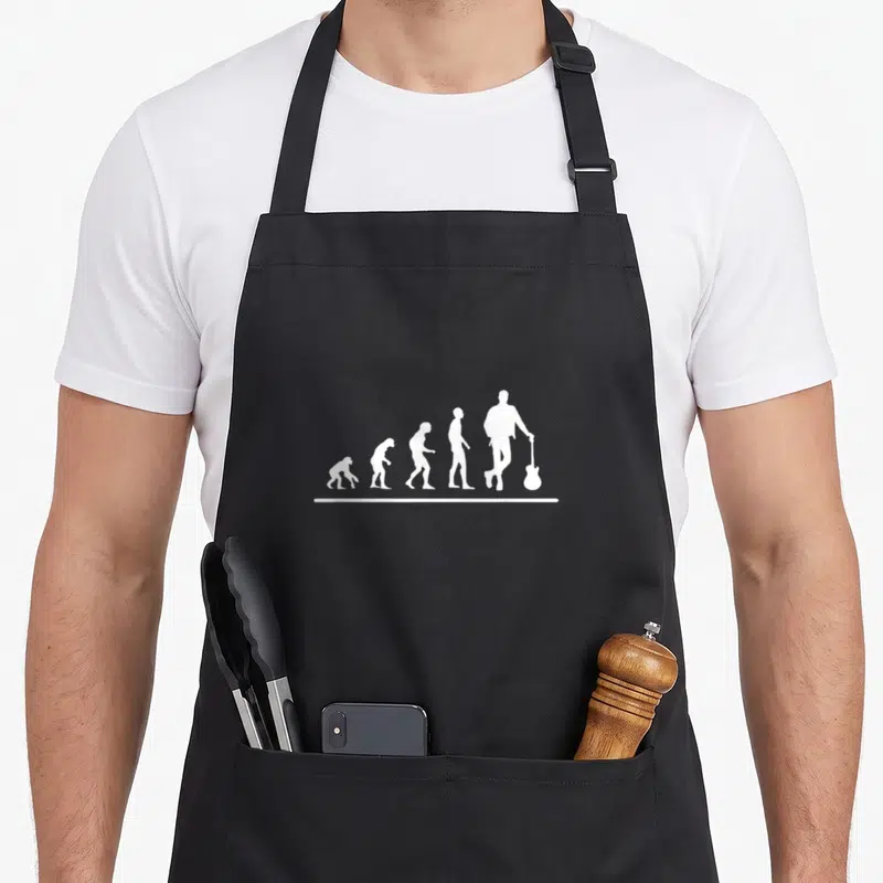 Tablier de cuisine noir avec une illustration blanche représentant l'évolution humaine se terminant par un homme tenant une guitare.